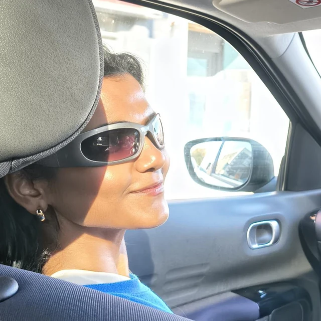 Kritika Singh, smiling in sunglasses in the front seat of a car on a sunny day.